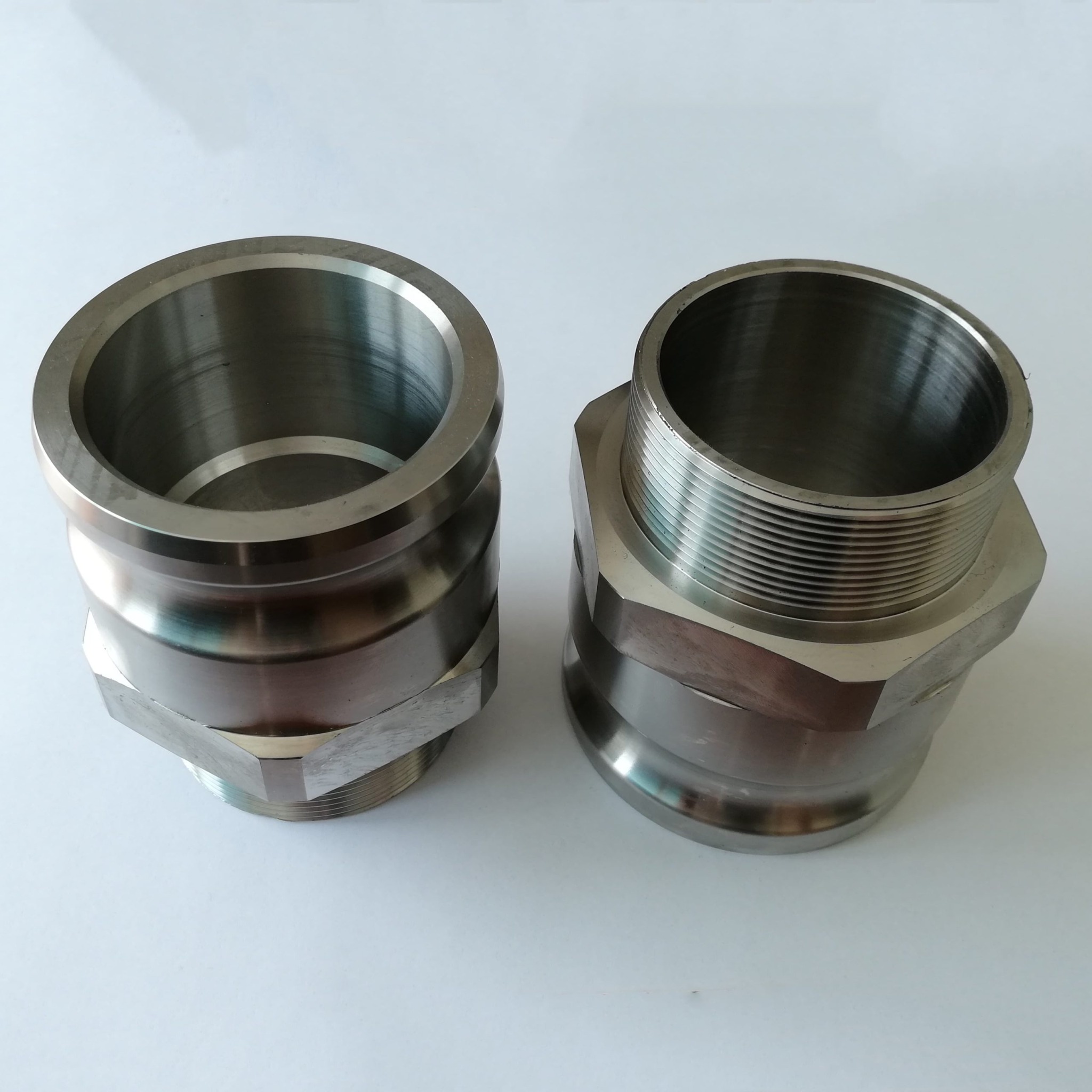 Dwa metalowe elementy z gwintem, wykonane w Katowicach, leżące na białym tle. Jeden element ma gładką powierzchnię, drugi posiada gwint na górnej części.