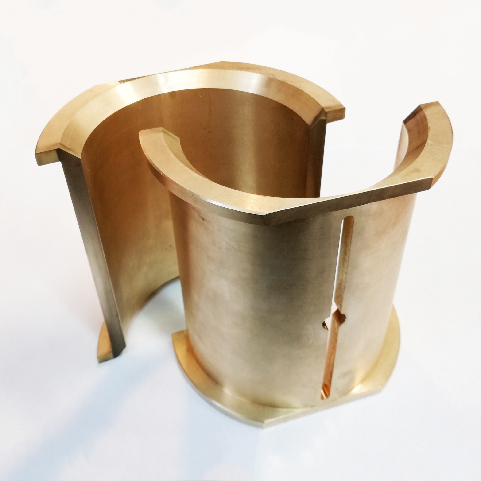 Dwa precyzyjnie obrobione, półokrągłe elementy z brązu, z widocznymi rowkami i krawędziami, ustawione na białym tle.