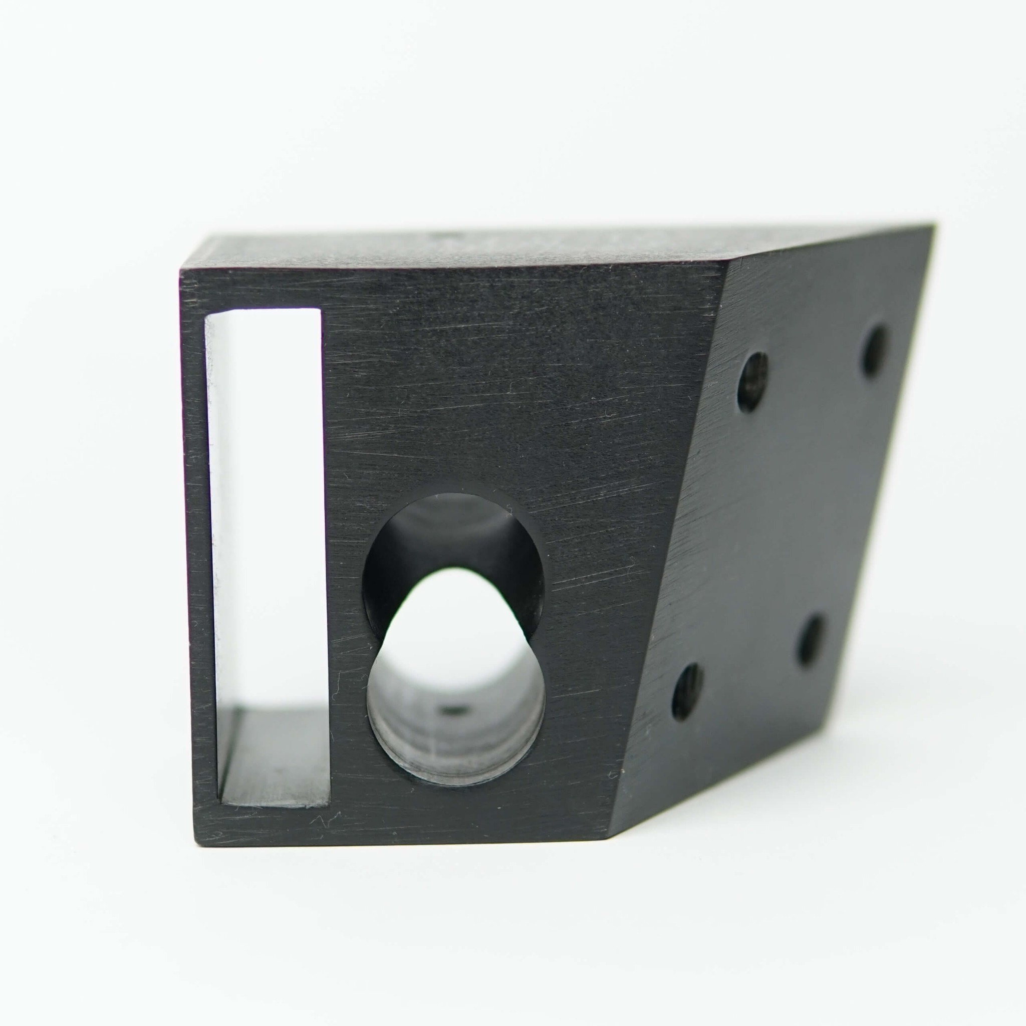 Czarny, matowy element metalowy z wyfrezowanymi otworami o różnych kształtach (prostokątny, okrągły) i nawierconymi otworami, leżący na białym tle.