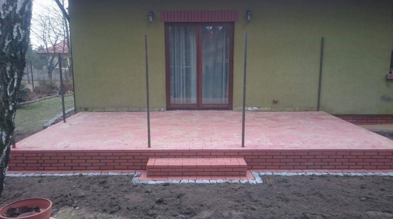 Nowy taras z czerwonej kostki brukowej z ceglanym obrzeżem i schodami, wykonany w Radomiu, z widocznymi przygotowaniami do montażu zadaszenia.