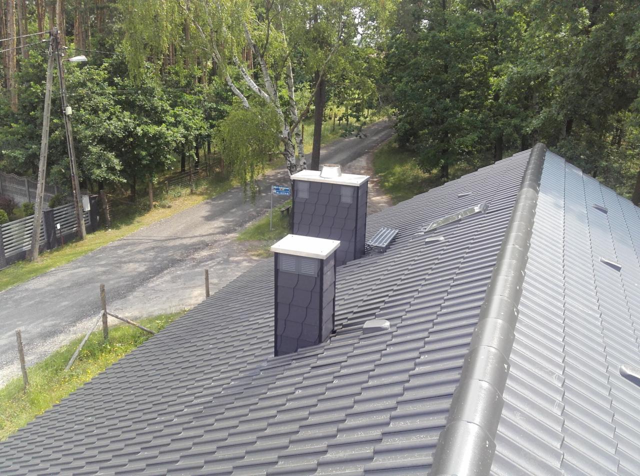 Nowy, grafitowy dach z dachówki ceramicznej z dwoma kominami w kolorze antracytu, widok z góry na tle lasu i drogi.