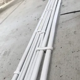 Wiązka białych kabli elektrycznych przymocowana do surowej betonowej ściany w Świdnicy, zabezpieczona białymi opaskami zaciskowymi.