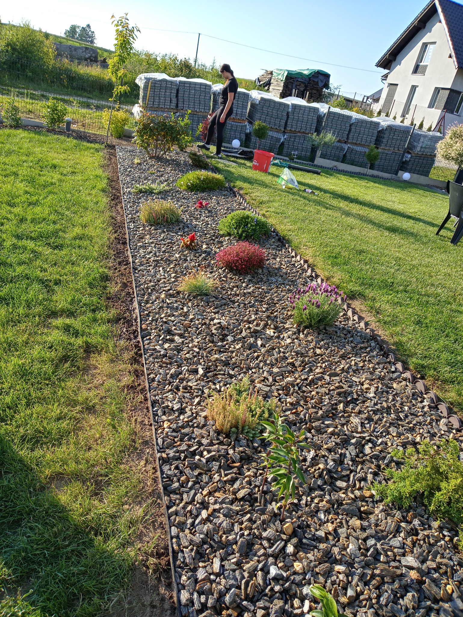 Rabata wysypana korą drzewną z posadzonymi roślinami, w tle ułożone kostki brukowe i osoba nadzorująca prace.