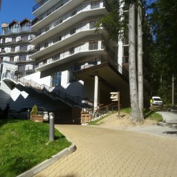 Przedsiębiorstwo Wielobranżowe MEGANT - Nowoczesny budynek apartamentowy z balkonami, widok z poziomu brukowanej ścieżki, zieleń i drzewa w otoczeniu. Jasne, słoneczne oświetlenie.