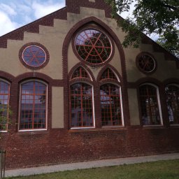 Przedsiębiorstwo Wielobranżowe MEGANT - Elewacja budynku z cegły i beżu z oknami w kolorze miedzi w Poznaniu. Okna prostokątne i okrągłe. Oryginalna architektura budynku.