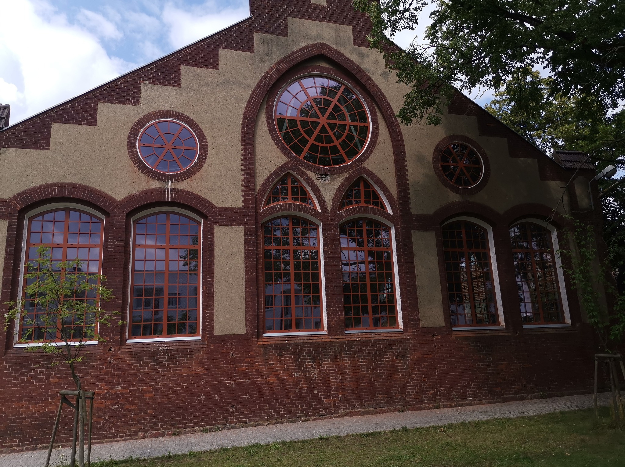 Elewacja budynku z cegły i beżu z oknami w kolorze miedzi w Poznaniu. Okna prostokątne i okrągłe. Oryginalna architektura budynku.
