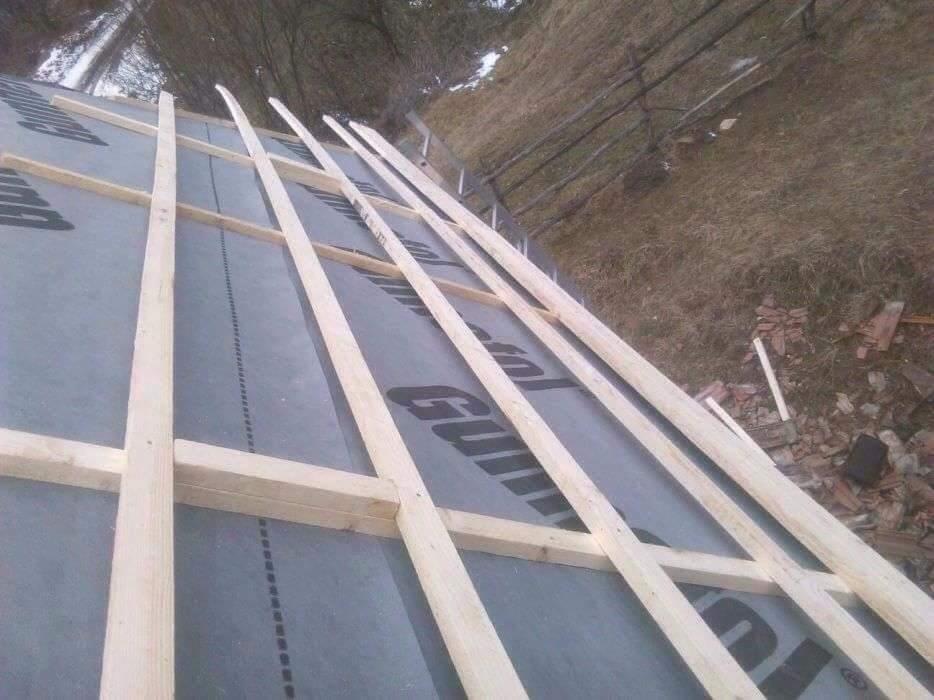 W trakcie budowy więźby dachowej w Kamiennej, widoczne drewniane elementy konstrukcyjne na membranie dachowej. Na skraju dachu leżą potłuczone dachówki.