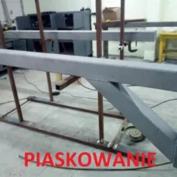 Trzy etapy obróbki metalu: spawanie surowej konstrukcji, element po piaskowaniu, element po malowaniu proszkowym, widoczne narzędzia i stanowiska pracy.