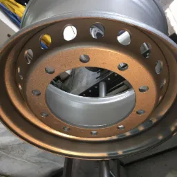 Obręcz koła ciężarówki po obróbce, z widoczną fakturą i kolorem nałożonej powłoki ochronnej, zawieszona na metalowej konstrukcji.