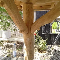 Konstrukcja drewniana z okrąglaków, prawdopodobnie fragment altany, widoczna butelka wody obok filaru.