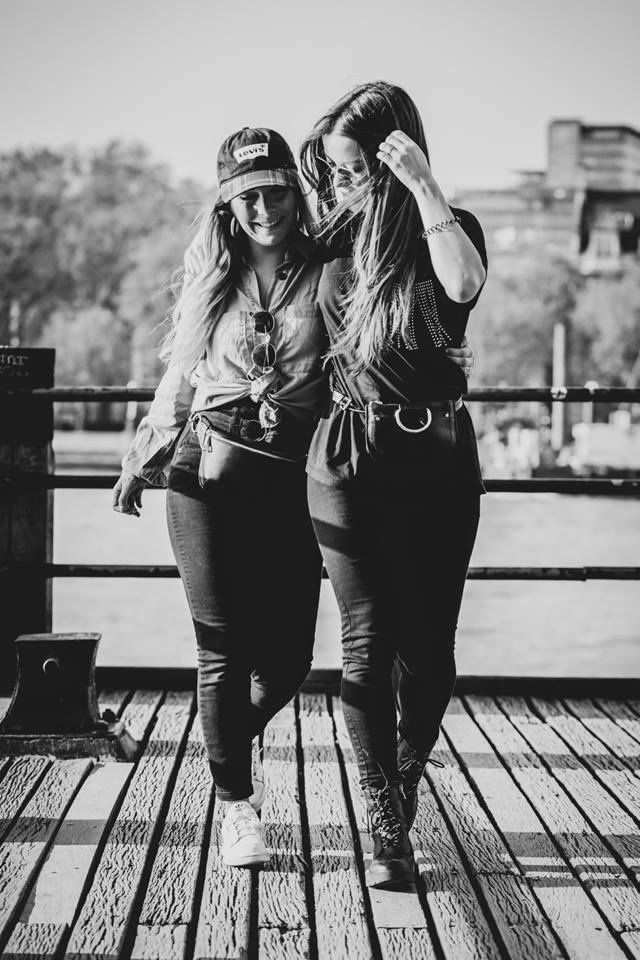 Dwie uśmiechnięte kobiety w casualowych ubraniach, stojące na drewnianym pomoście w słoneczny dzień, zdjęcie czarno-białe z perspektywy lekko z dołu.