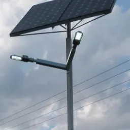 Słup oświetleniowy z panelem słonecznym i dwiema lampami LED na tle pochmurnego nieba z liniami energetycznymi.