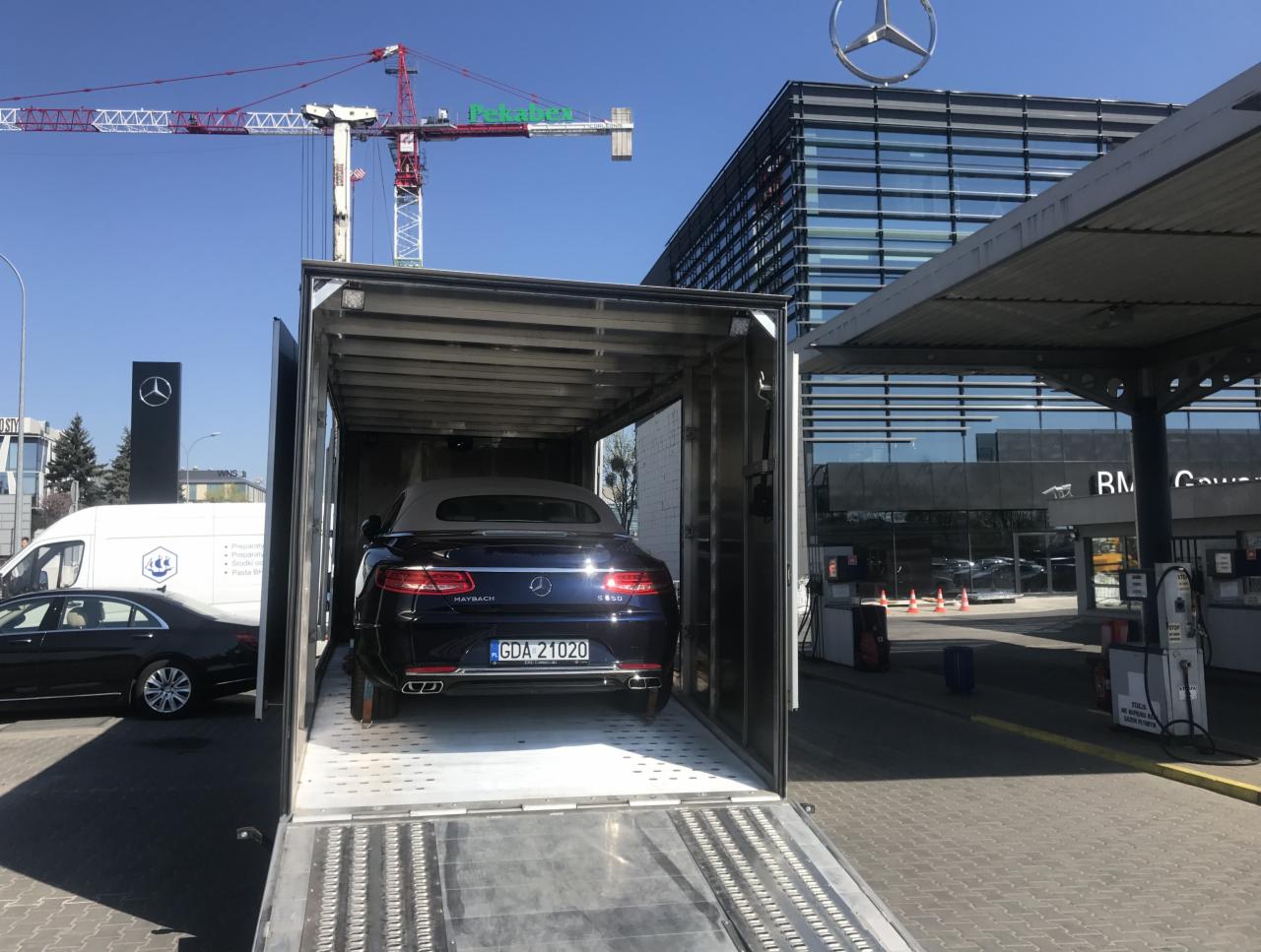 Czarny Maybach S650 z otwartym dachem wewnątrz aluminiowej lawety na tle budynku salonu Mercedesa i żurawia budowlanego.