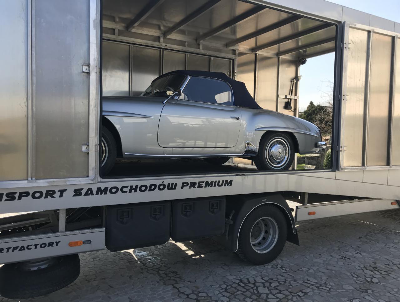 Srebrny zabytkowy kabriolet Mercedes-Benz 190 SL z czarnym dachem wewnątrz aluminiowej zabudowy lawety z napisem 'TRANSPORT SAMOCHODÓW PREMIUM'.