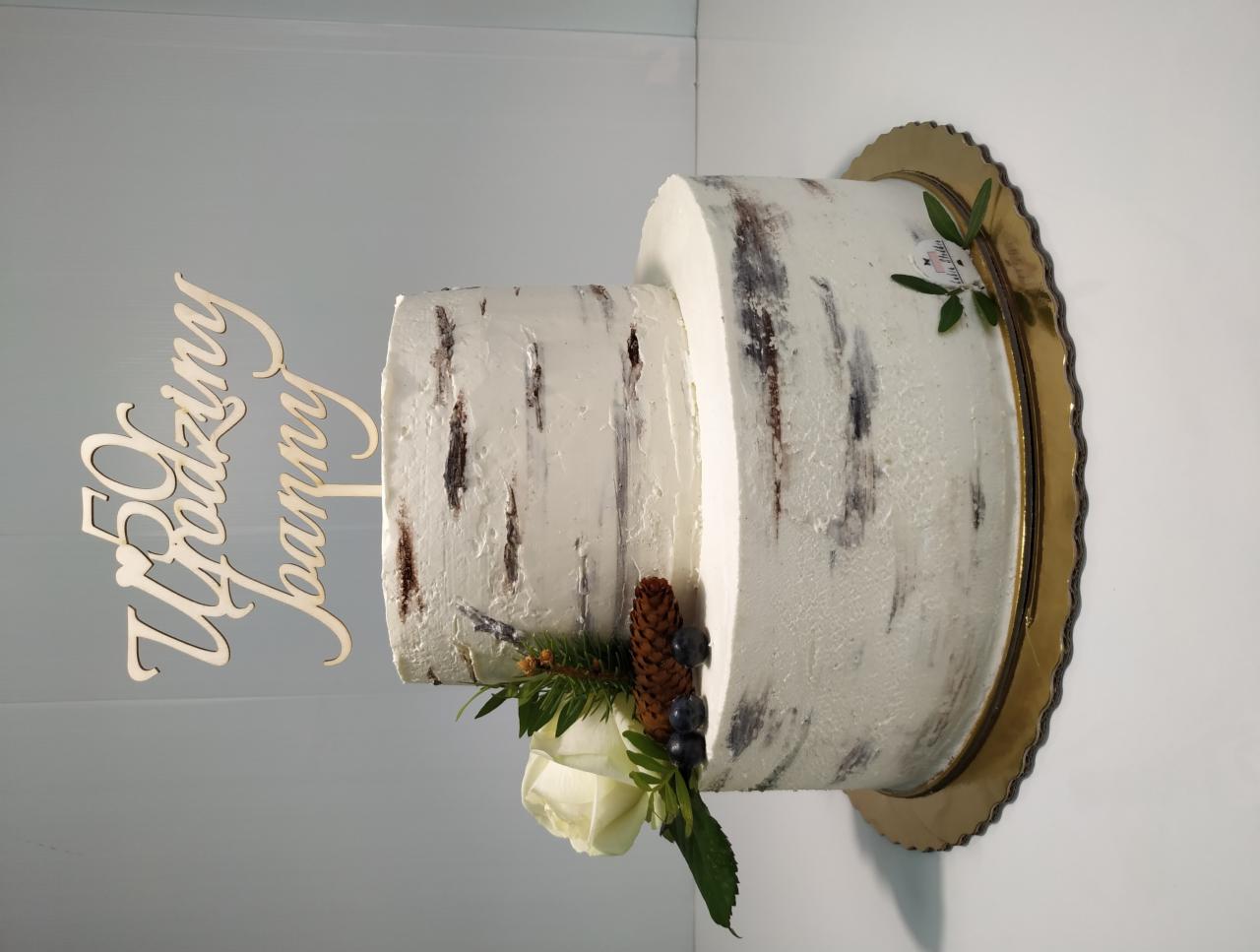 Dwupoziomowy tort weselny z kremem imitującym korę brzozy, ozdobiony białą różą, szyszką i napisem '50 Rodziny Joanny'.