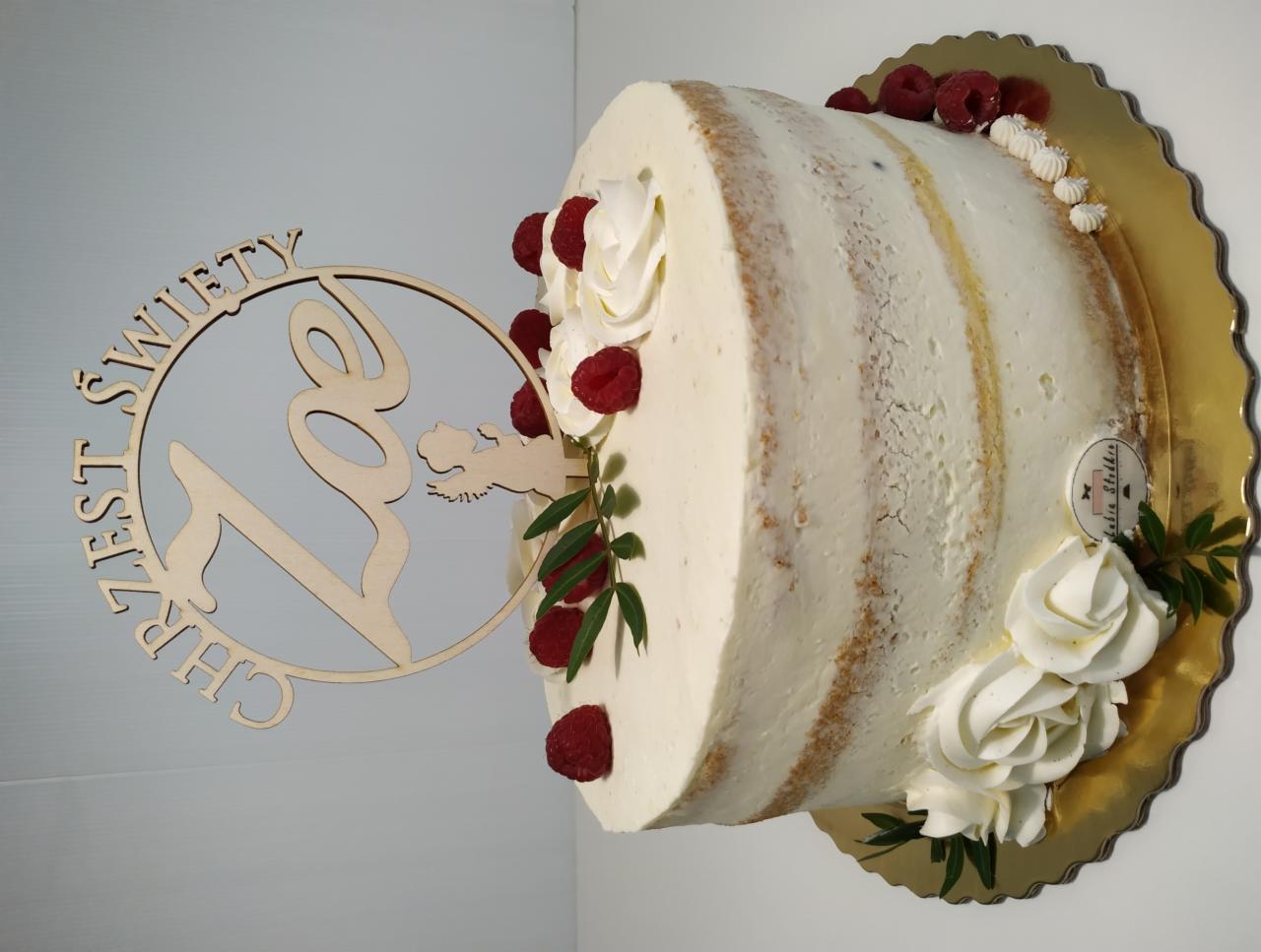 Tort z kremem, malinami i drewnianym topperem 'Chrzest Święty Zoi', umieszczony na złotej podkładce.