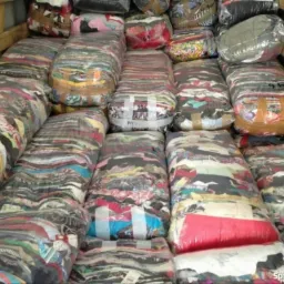 Bale sprasowanej, używanej odzieży damskiej i męskiej, owinięte folią i taśmą, ułożone w magazynie lub kontenerze.