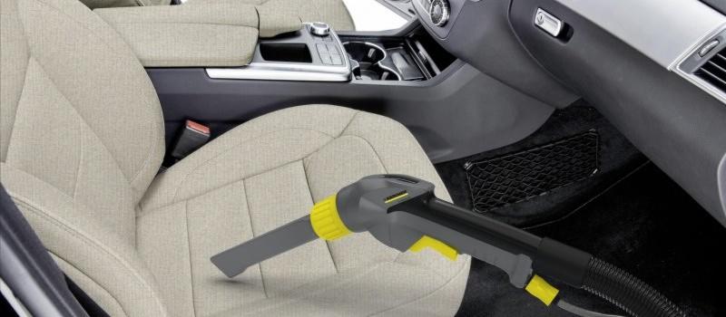 Szczegółowe ujęcie czyszczenia beżowego fotela samochodowego odkurzaczem parowym Karcher z żółtymi akcentami, widoczna struktura materiału i siatka w kieszeni bocznej.