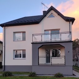 ZHUP Sima Marcin Siekierski - Dwukondygnacyjny dom z beżową elewacją, czarnym dachem i balkonem z balustradą szklaną na pierwszym piętrze, widok z zewnątrz o zmierzchu.