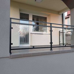 ZHUP Sima Marcin Siekierski - Nowoczesna balustrada balkonowa ze szkła i czarnej stali, widok z zewnątrz, szare płytki na balkonie.