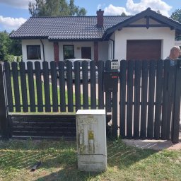 ZHUP Sima Marcin Siekierski - Ciemnoszare ogrodzenie panelowe z metalowymi sztachetami i elementami imitującymi cegłę, przed domem z garażem i tabliczką 'Uwaga zły pies'.