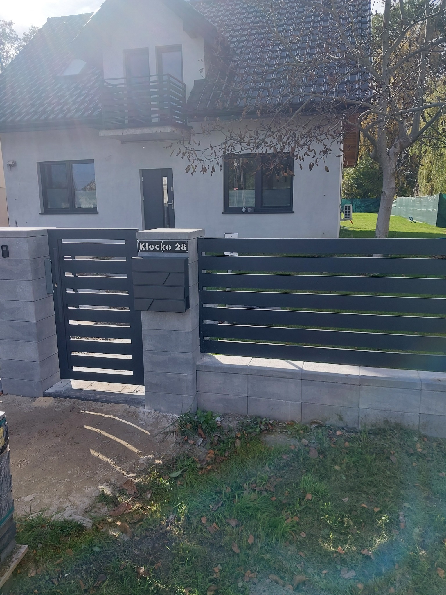Nowoczesna, pozioma brama wjazdowa z szarego metalu i kamienne słupki w Izabelowie, zintegrowana ze skrzynką na listy i numerem domu.