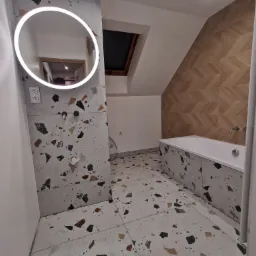 Nowoczesna łazienka na poddaszu z terazzo na ścianach i podłodze, owalnym lustrem z podświetleniem LED, drewnianą ścianą w jodełkę i oknem dachowym.