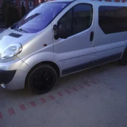 Srebrny Opel Vivaro z przyciemnianymi szybami i czarnymi felgami, zaparkowany na chodniku z czerwonymi akcentami.