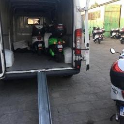 GlobalTrick - Biały bus z otwartymi drzwiami ładunkowymi i rampą załadunkową; wewnątrz skutery elektryczne, a na zewnątrz zaparkowane inne skutery.