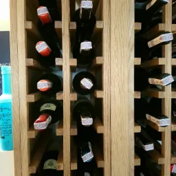 Ręcznie wykonany drewniany regał na wino z różnymi butelkami, widoczne detale konstrukcyjne i naturalne usłojenie drewna.