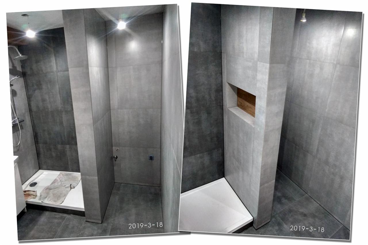 Wykończona kabina prysznicowa z szarymi, matowymi płytkami wielkoformatowymi, biały brodzik, półka wbudowana w ścianę wykończona drewnem, oświetlenie punktowe.