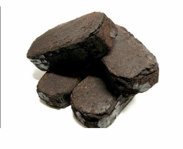 Brykiety węgla drzewnego ułożone w stos na białym tle, widoczne nieregularne krawędzie i struktura węgla.
