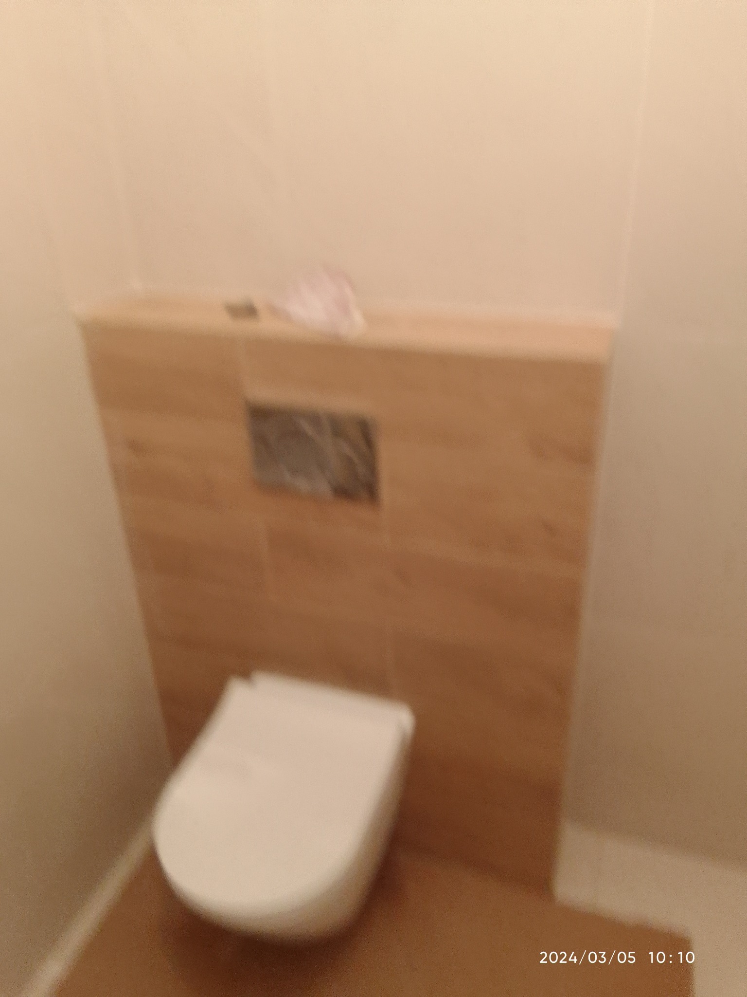 Zamontowana toaleta podwieszana z zabudową z płytek imitujących drewno w jasnej łazience.