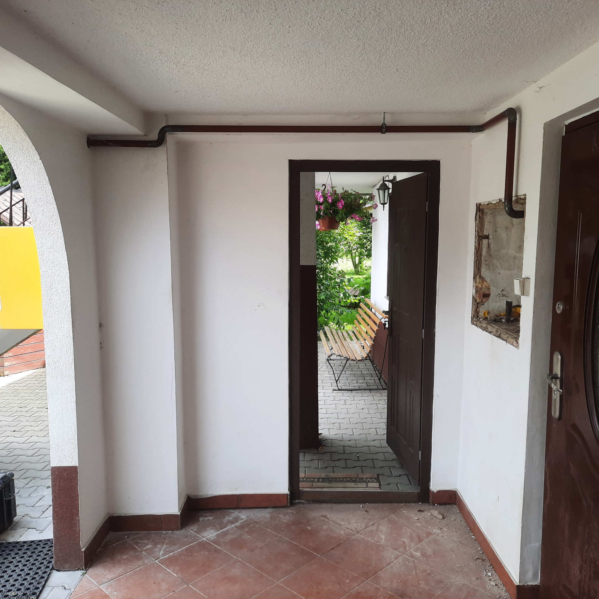 Brązowe rury instalacji gazowej poprowadzone wzdłuż sufitu i ścian w korytarzu domu, widoczna otwarta przestrzeń z roślinami i ławką.