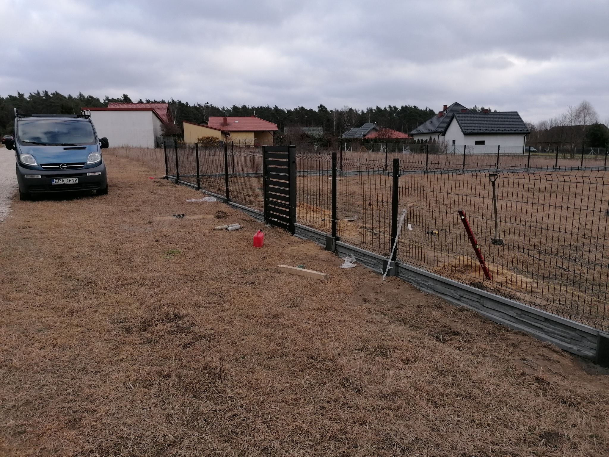 W trakcie instalacji ogrodzenia panelowego z podmurówką betonową; widoczny samochód dostawczy firmy na tle domów jednorodzinnych.