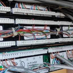 Panel krosowniczy z podłączonymi kablami sieciowymi, widoczne oznaczenia kategorii Cat. 5E oraz numery portów.