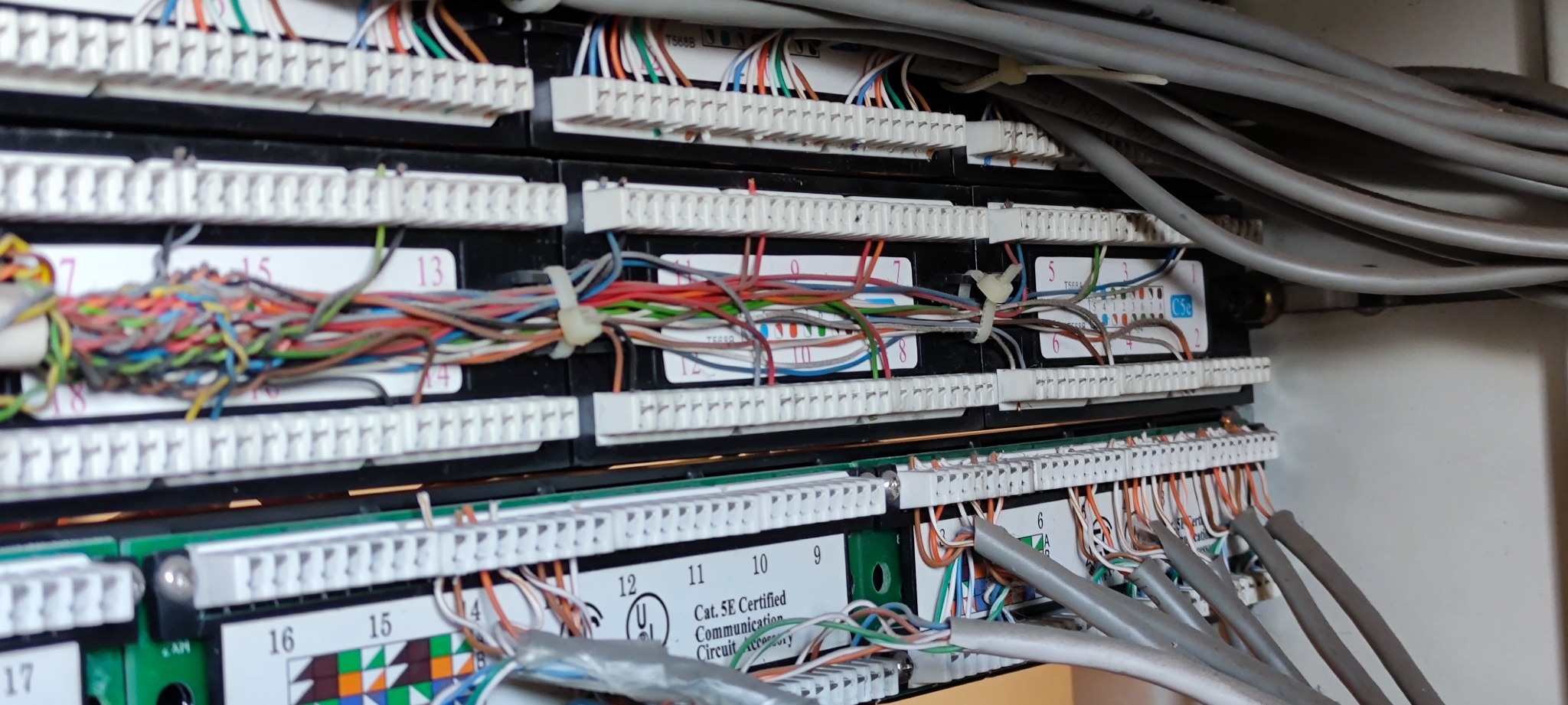 Panel krosowniczy z podłączonymi kablami sieciowymi, widoczne oznaczenia kategorii Cat. 5E oraz numery portów.