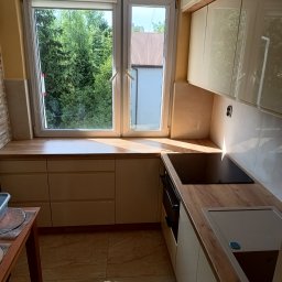 Maryka Ryszard Kapałka - Jasna, nowoczesna kuchnia z drewnianymi blatami, widok na zieleń za oknem, płyta indukcyjna i zintegrowany z blatem zlew.