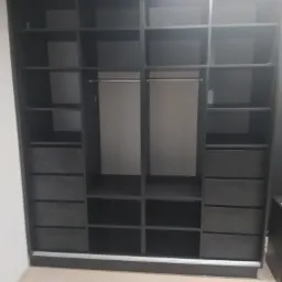 Ciemnoszara szafa wnękowa z przesuwnymi drzwiami, widoczne półki i szuflady, puste wnętrze, minimalistyczny design.