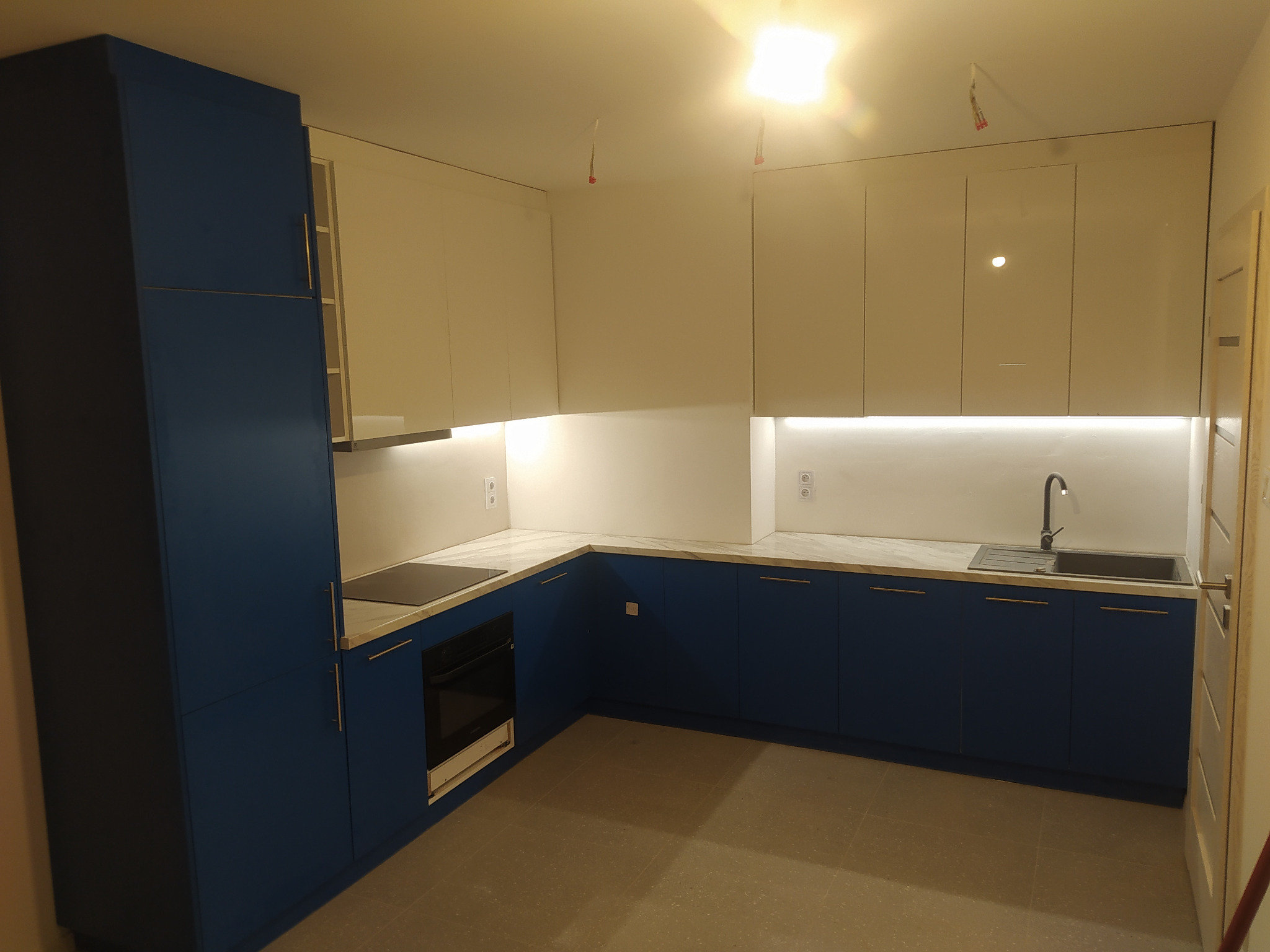 Nowoczesna kuchnia w Tarnowie z granatowymi dolnymi szafkami i białymi górnymi, wykończona blatem imitującym marmur, oświetlenie LED pod szafkami, piekarnik w zabudowie.