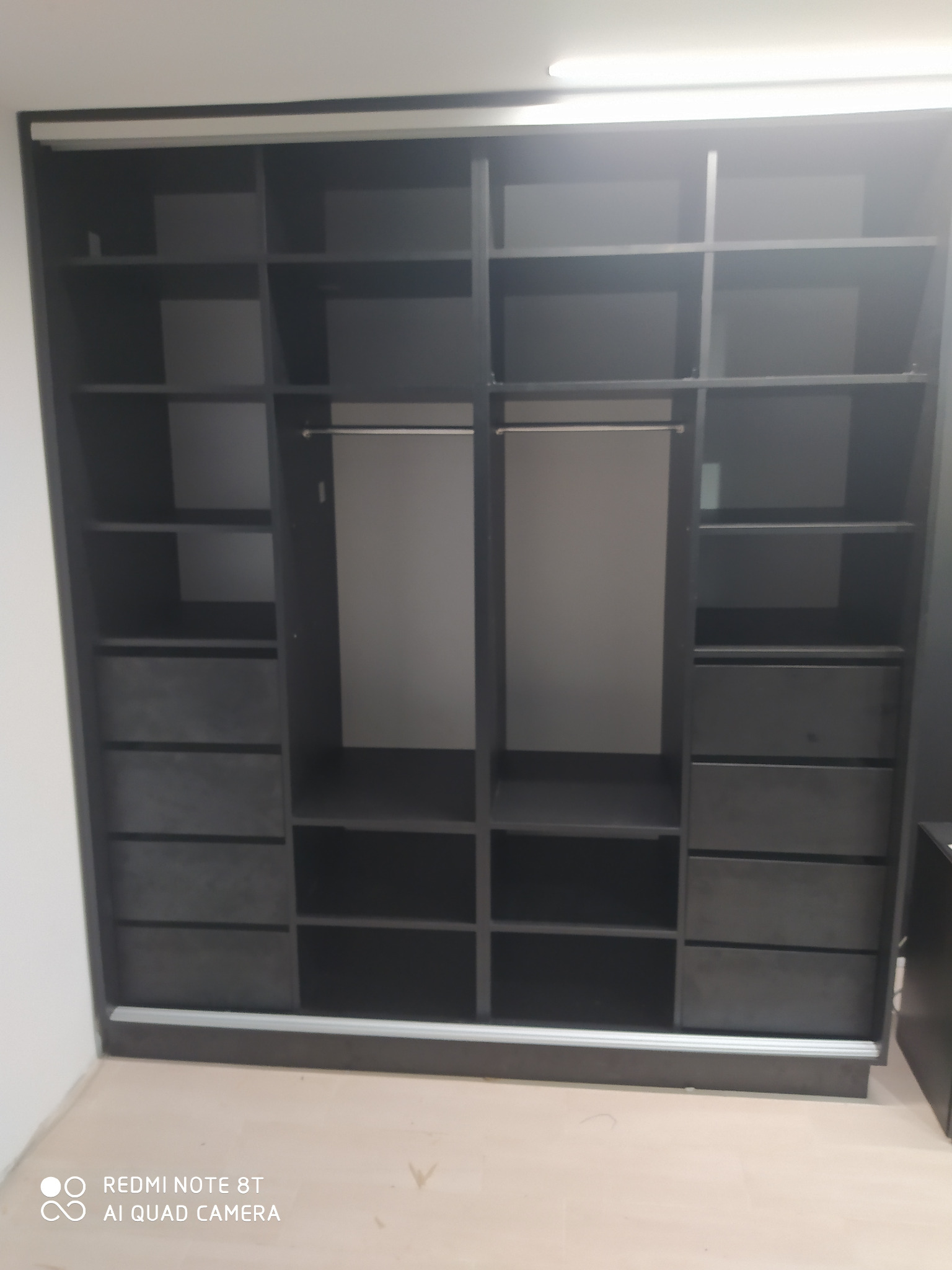 Ciemnoszara szafa wnękowa z przesuwnymi drzwiami, widoczne półki i szuflady, puste wnętrze, minimalistyczny design.