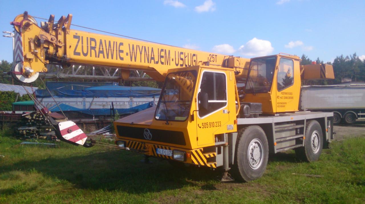 Żółty dźwig samochodowy z napisem 'Żurawie-Wynajem-Usługi 25T' na wysięgniku, stojący na trawiastym terenie w słoneczny dzień.