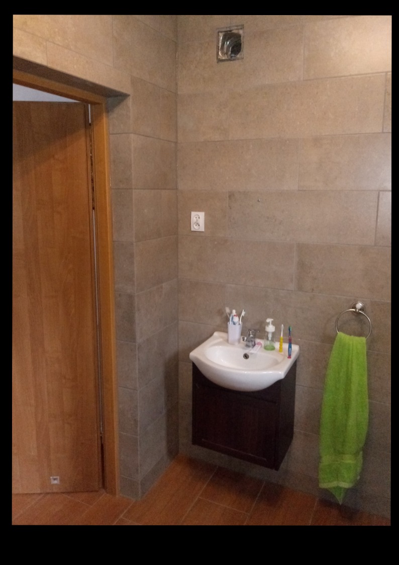 Umywalka z szafką w wykończonej łazience, jasne płytki na ścianach, widoczny wieszak na ręcznik z zielonym ręcznikiem.