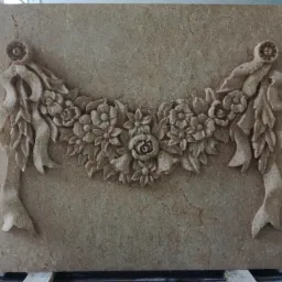 Płaskorzeźba z piaskowca przedstawiająca girlandę kwiatową z wstążkami, umieszczona na palecie transportowej.