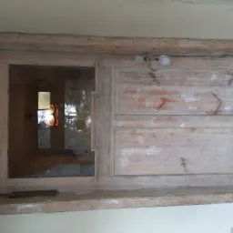 Stare drewniane okno z częściowo usuniętą farbą, widoczne ślady po szpachlowaniu, z zewnątrz widać odbicie lampy i okna w szybie.