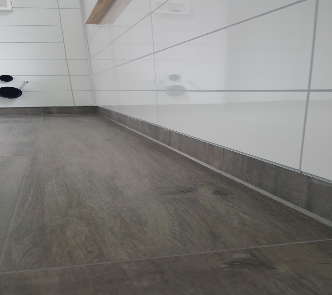 Wykończona łazienka z drewnopodobną podłogą i białymi płytkami ściennymi z szarą listwą przypodłogową i elementami instalacji sanitarnej.