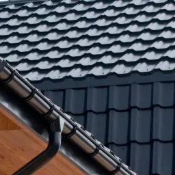 Czarne, metalowe rynny i ciemnoszare pokrycie dachowe z blachy na drewnianej podbitce dachowej.