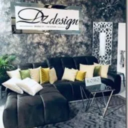 Ciemna, welurowa sofa narożna z dekoracyjnymi poduszkami w odcieniach bieli, zieleni i żółci, ustawiona w nowoczesnym wnętrzu z szarą, teksturowaną ścianą i lustrzaną dekoracją oraz stolikiem...