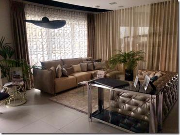 Elegancki salon z beżowym narożnikiem, wzorzystymi zasłonami w odcieniach beżu i brązu, oraz dekoracyjnym oświetleniem i roślinami doniczkowymi.