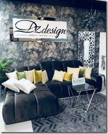 Ciemna, welurowa sofa narożna z dekoracyjnymi poduszkami w odcieniach bieli, zieleni i żółci, ustawiona w nowoczesnym wnętrzu z szarą, teksturowaną ścianą i lustrzaną dekoracją oraz stolikiem...